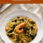 A bowl of spaghetti with prawns and zucchini served alongside white wine and fresh whole prawns.