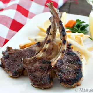 Close-up of grilled lamb cutlets with char marks, served with fries and lemon.