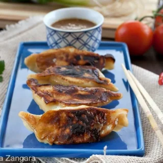 Pan-fried Kothey Momos served on a plate with tomato chutney and chopsticks.