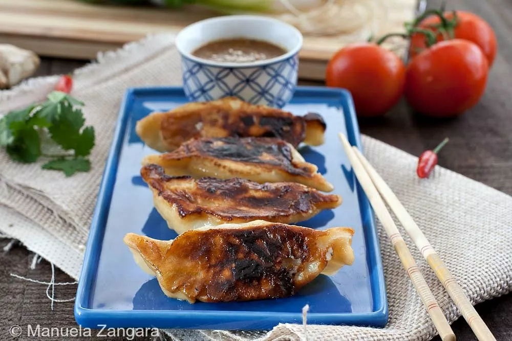 Pan-fried Kothey Momos served on a plate with tomato chutney and chopsticks.