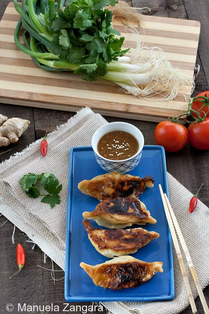 Kothey Momos served on a blue plate with tomato chutney, fresh coriander, and spring onions in the background.