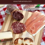 Tigelle Bread served with salami, prosciutto and cheese on a wooden board.