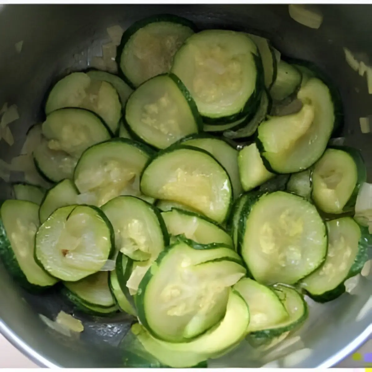 Cooked zucchini slices with sautéed onions in a pot.