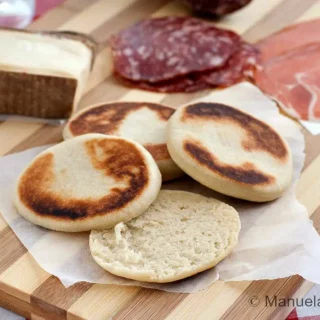 Tigelle Bread served with salami, prosciutto and cheese on a wooden board.