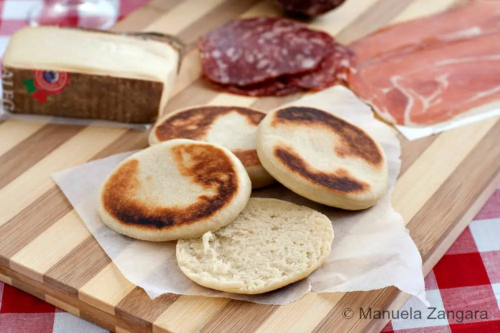 Tigelle Bread served with salami, prosciutto and cheese on a wooden board.