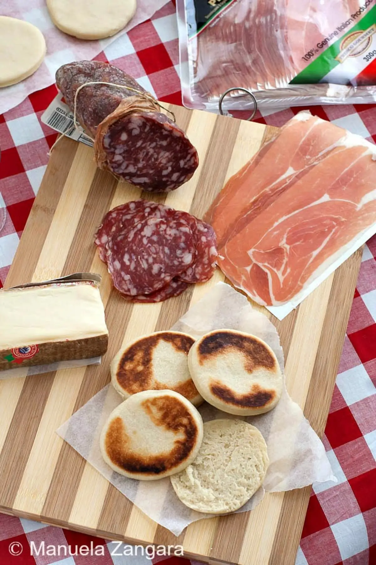 Tigelle Bread served with salami, prosciutto and aged cheese on a wooden board.