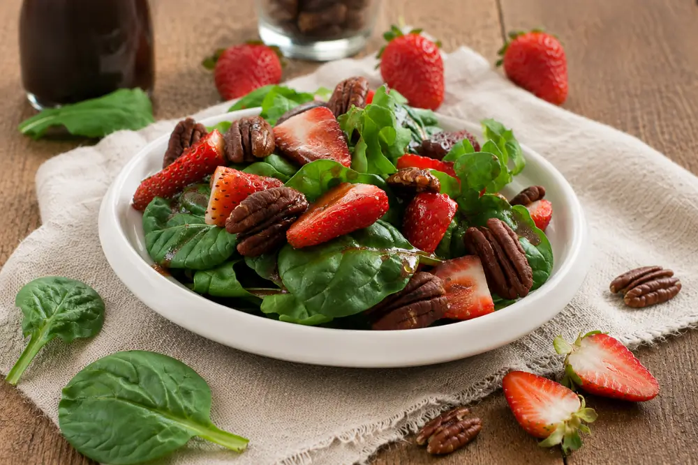 A serving bowl of rocket and spinach salad with fresh strawberries, toasted pecans and homemade strawberry dressing.
