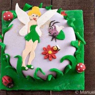 Full view of the Tinkerbell fondant cake with green base and character decorations.