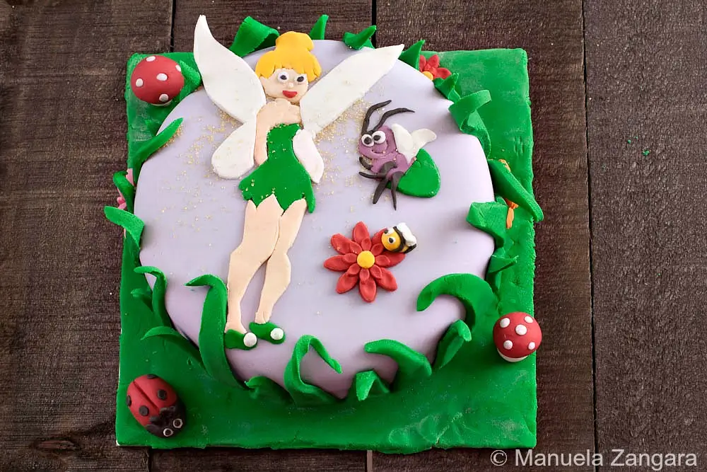 Full view of the Tinkerbell fondant cake with green base and character decorations.