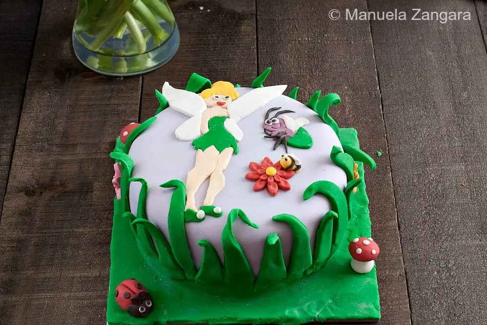 Tinkerbell cake decorated with fondant grass, mushrooms and small insects.