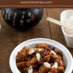 Ginger Sesame Chicken garnished with spring onions and dried chilli in a white bowl.