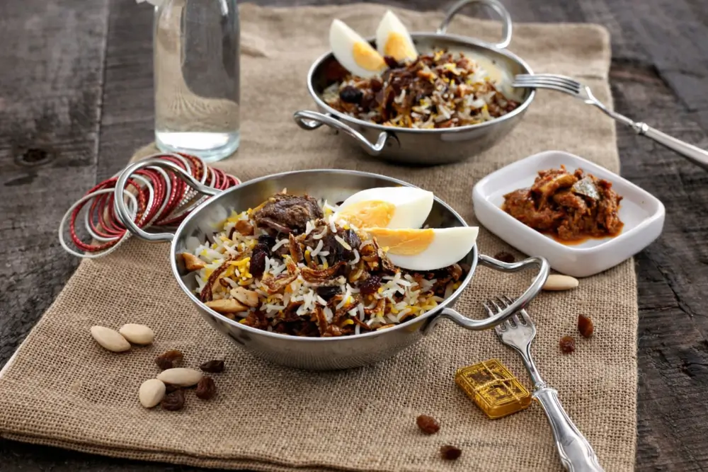 Indian lamb biryani plated with boiled eggs, nuts, and a side of pickle.