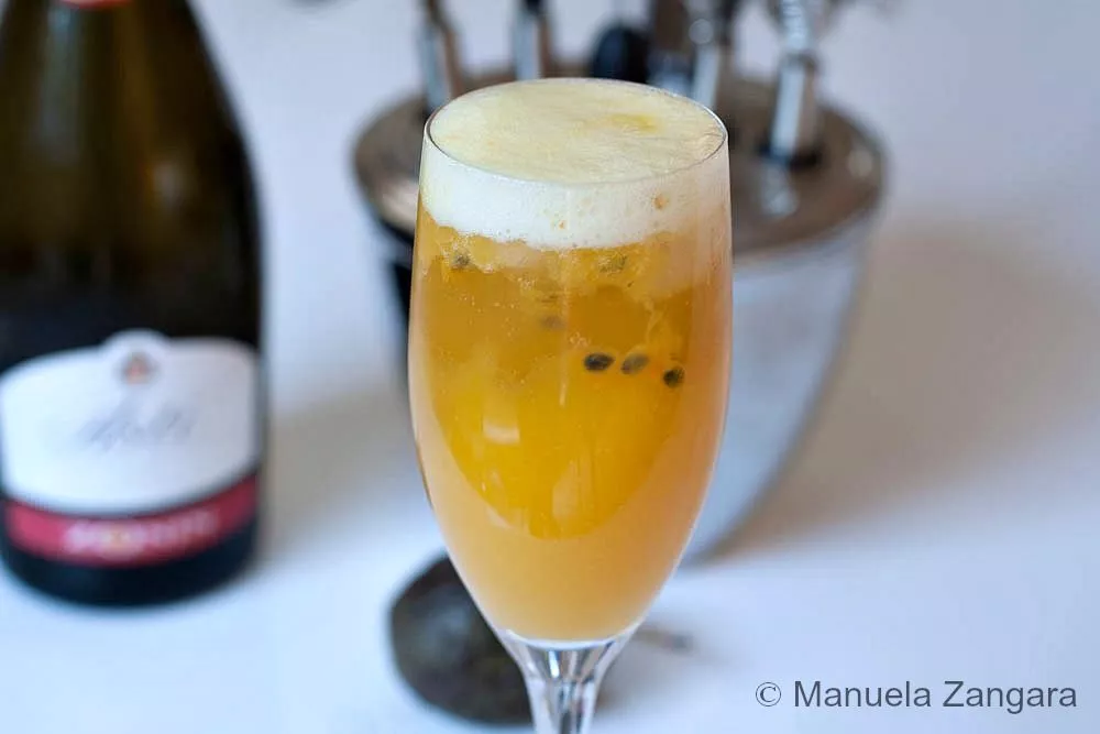 Close-up of a mango and passion fruit cocktail in a Champagne flute showing the passion fruit seeds and frothy top.