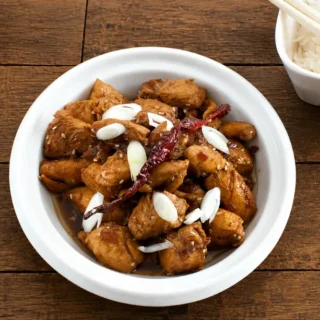 Ginger Sesame Chicken served with steamed rice and chopsticks on a wooden table.