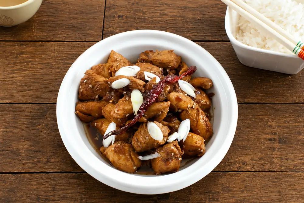Ginger Sesame Chicken served with steamed rice and chopsticks on a wooden table.