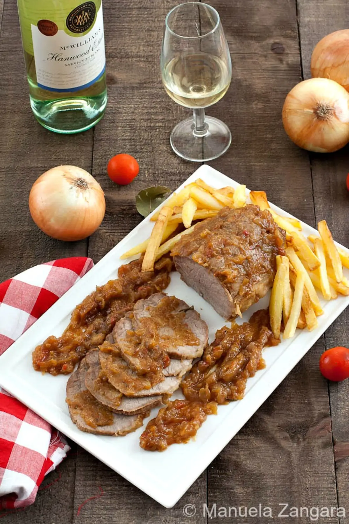 Sliced beef roast served with onion glaze and fries on a white platter.