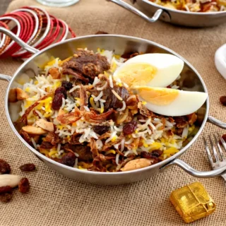 Indian biryani topped with nuts, sultanas, and fried onions on a rustic table.