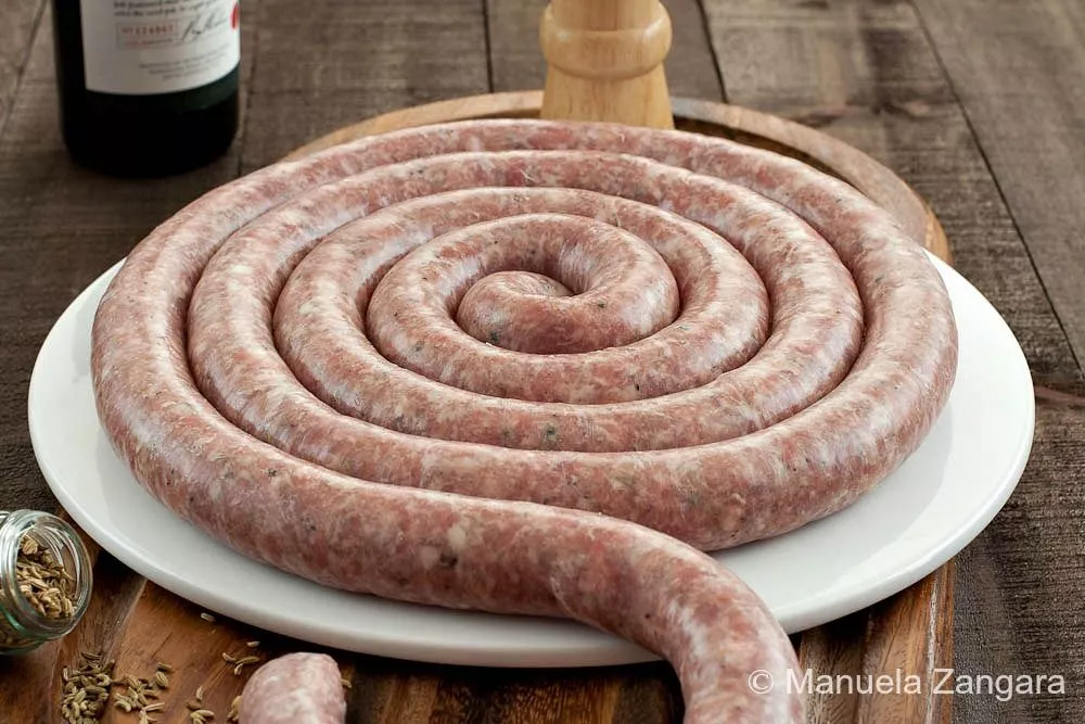 Homemade Italian fennel sausage on a wooden cutting board with spices and fennel seeds.