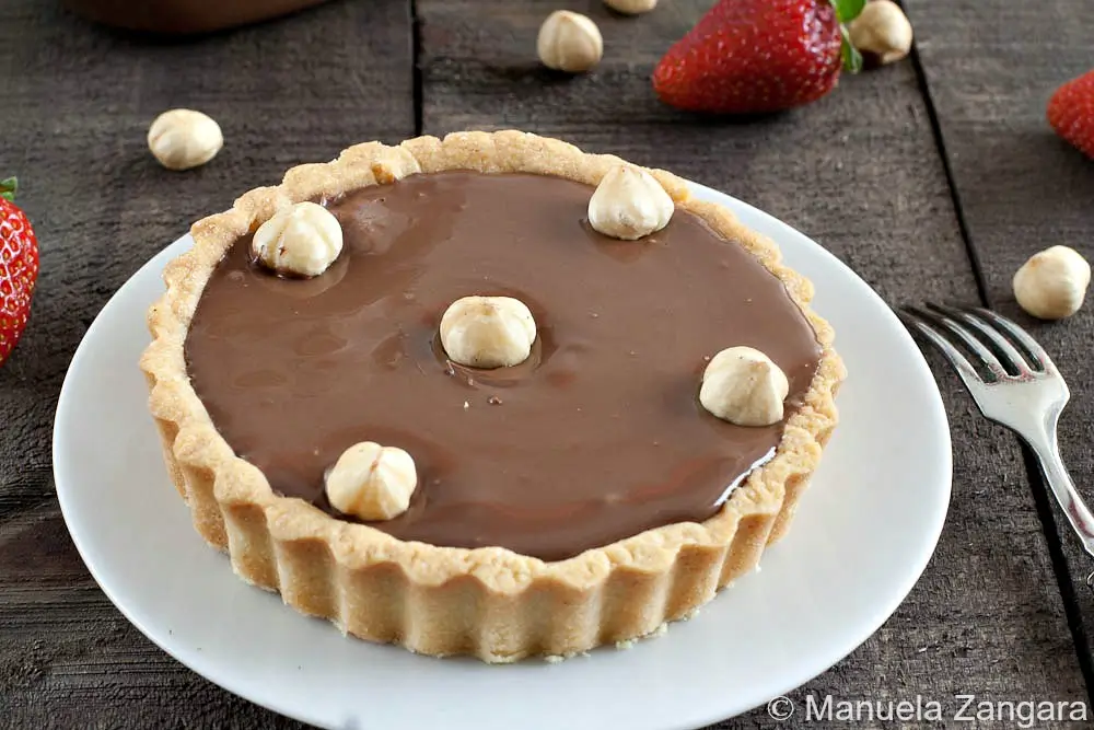 Close-up of a Nutella tart topped with whole hazelnuts.