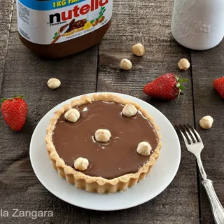Tart with Nutella on a plate with hazelnuts and strawberries around it.
