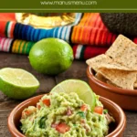 Homemade guacamole served in a bowl with lime wedges and tortilla chips on the side.