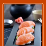 Homemade Salmon Nigiri served on a black rectangular plate with sushi rice, soy sauce, and pickled ginger.