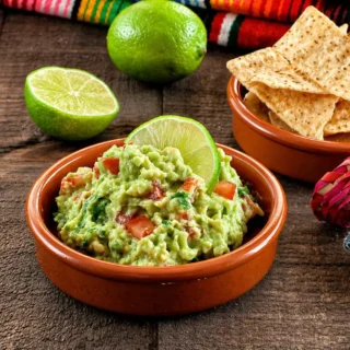Fresh guac served in a bowl with tortilla chips and lime on the side.