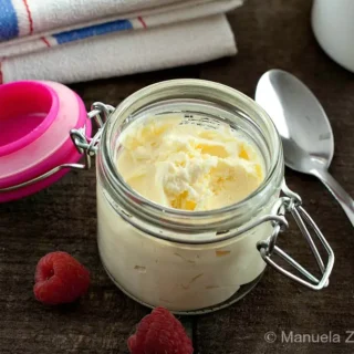 Spoonful of creamy homemade mascarpone in a glass jar with fresh raspberries.