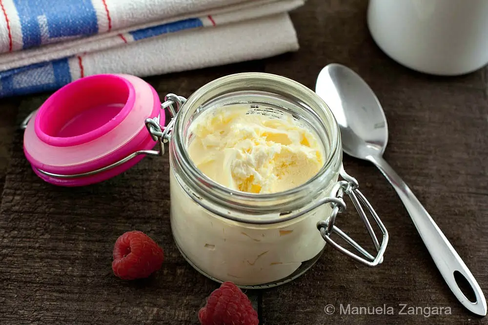 Spoonful of creamy homemade mascarpone in a glass jar with fresh raspberries.