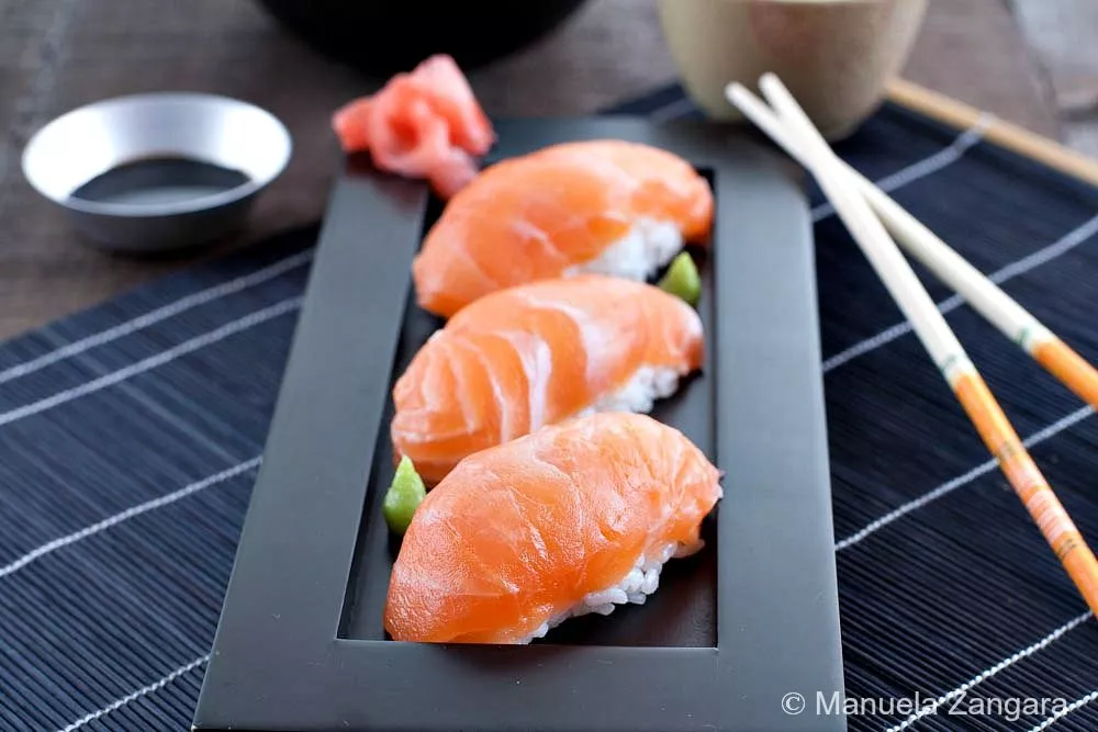Homemade Salmon Nigiri served on a black rectangular plate with sushi rice, soy sauce, and pickled ginger.