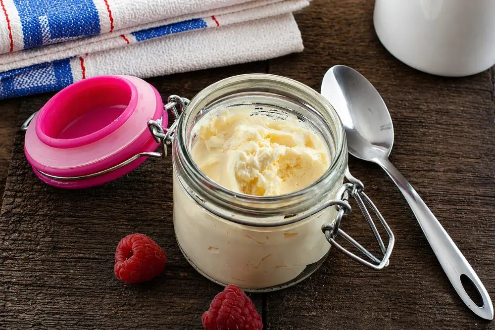 Creamy mascarpone in a small glass jar beside raspberries and a spoon.