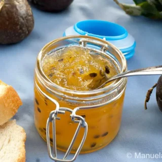 Close-up of a jar filled with glossy pineapple and passion fruit jam beside sliced bread.