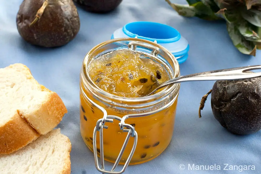 Close-up of a jar filled with glossy pineapple and passion fruit jam beside sliced bread.