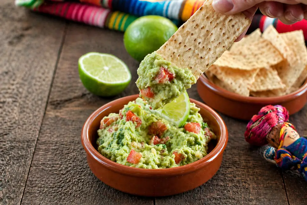 Tortilla chip dipped into creamy guac with visible tomato and herbs.
