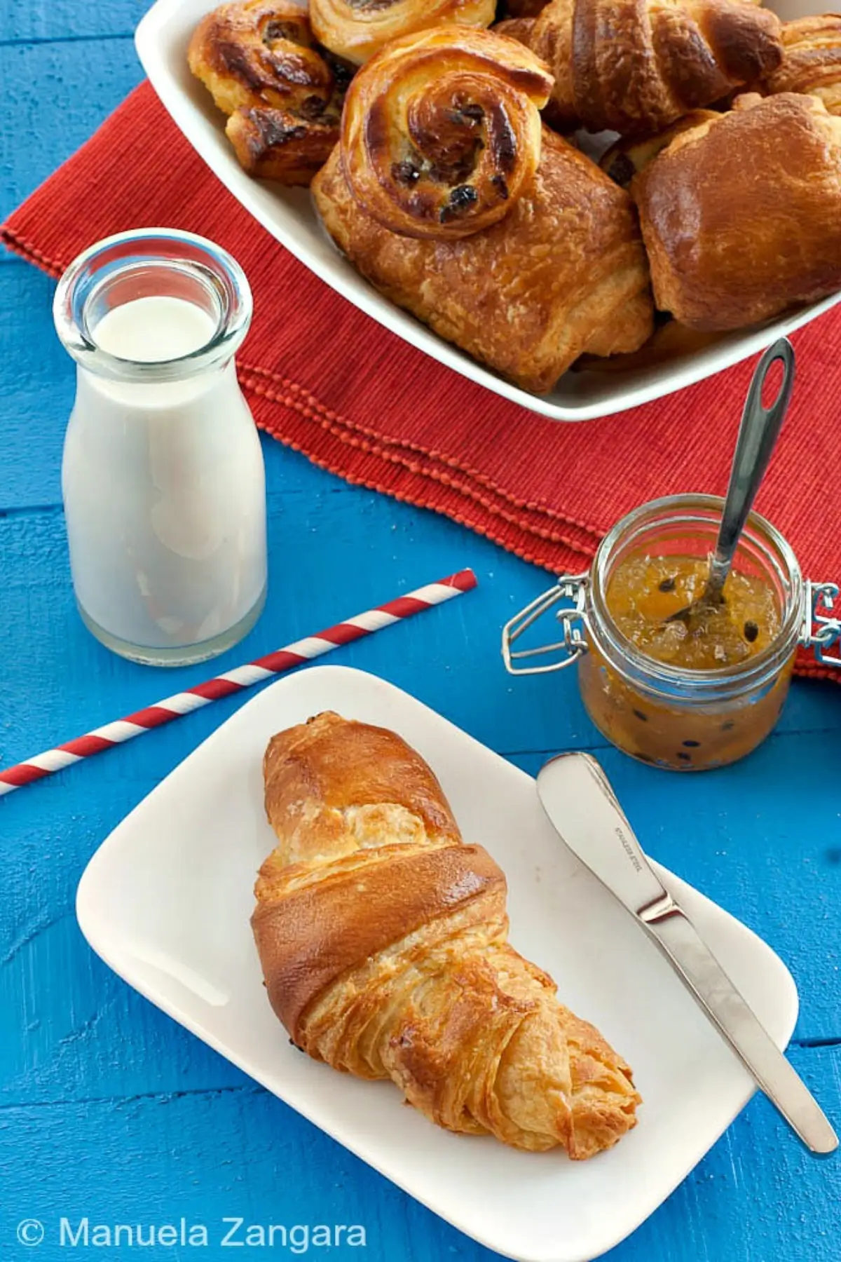 Golden croissant served on a plate with visible flaky layers.