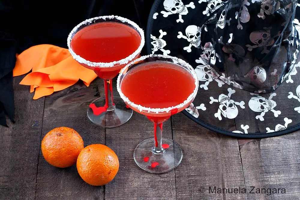 Two Blood Orange Margaritas with salted rim and oranges on table.