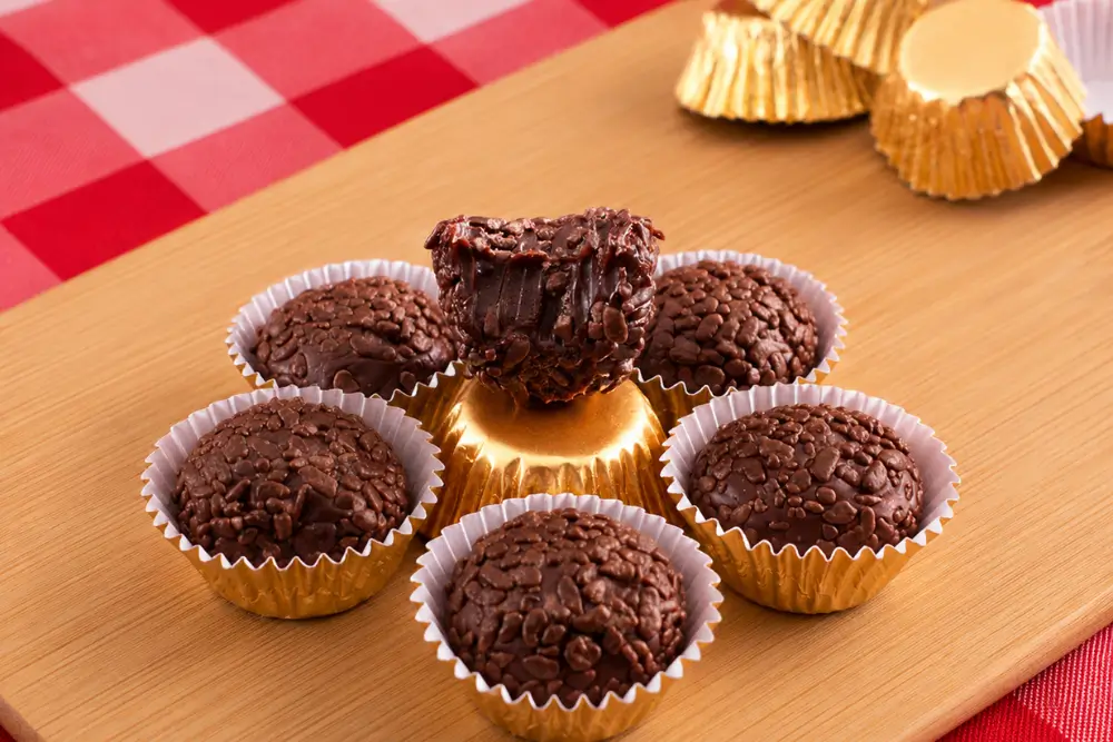Brigadeiros arranged in paper cups on a bamboo board with a red gingham cloth background.