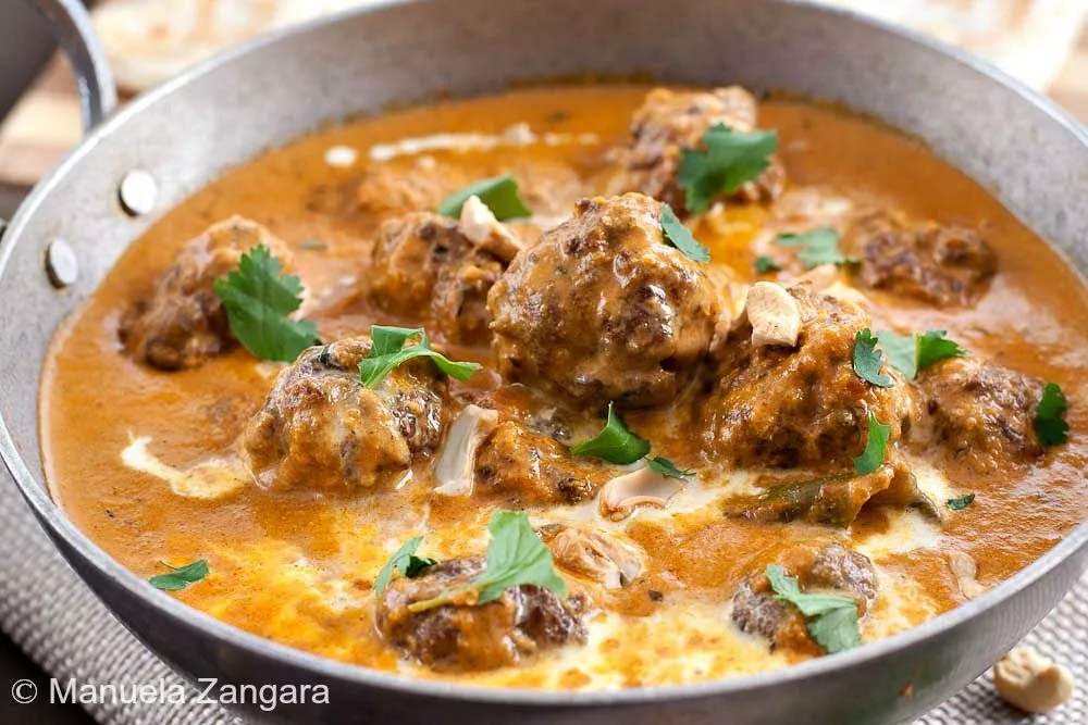 Close-up of lamb koftas in creamy curry sauce, garnished with cilantro.