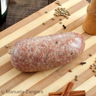 Close-up shot of an uncooked cotechino on a wooden board with spices scattered nearby.