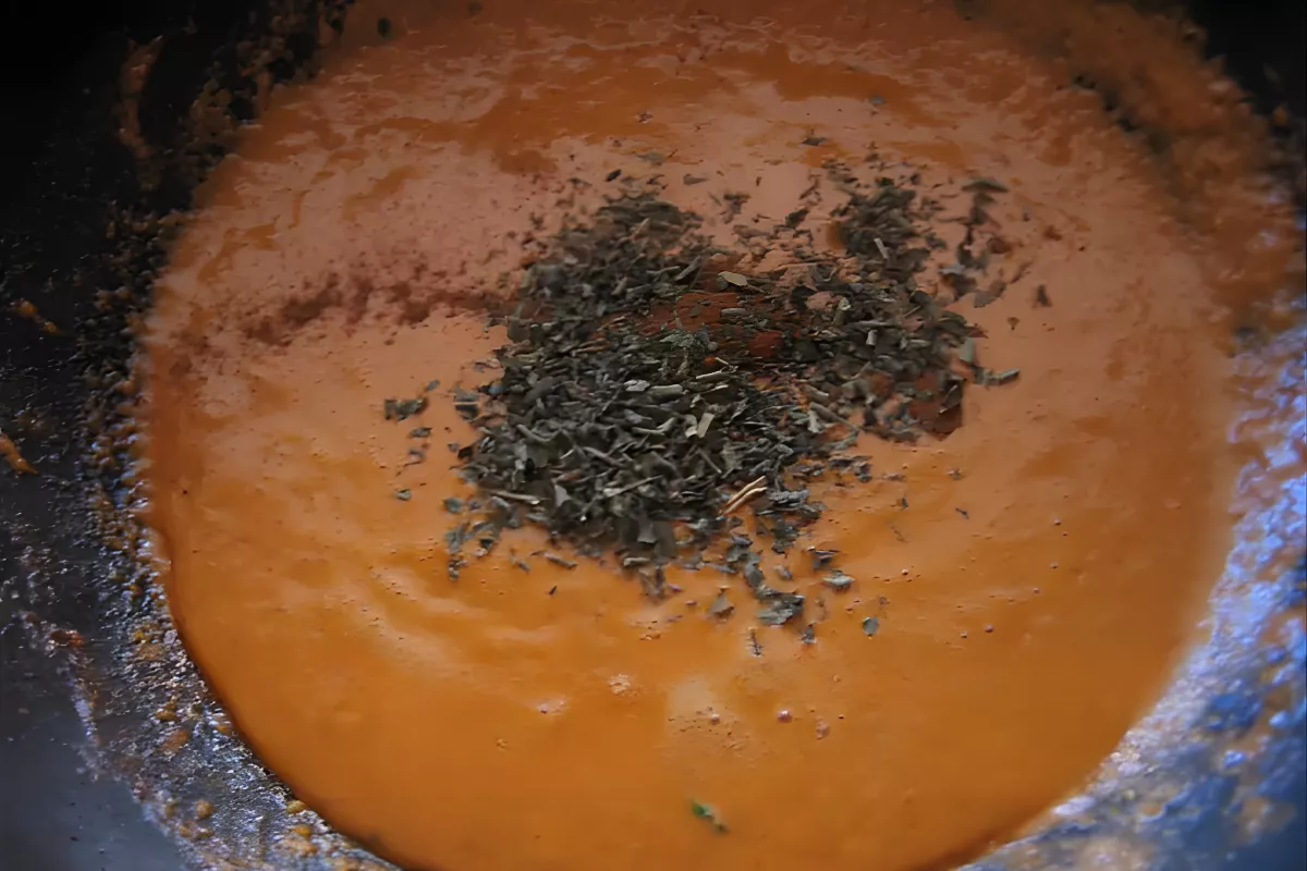 Spiced curry sauce with herbs being stirred in.