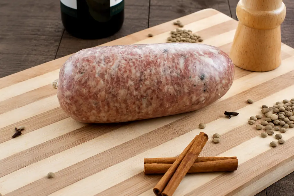 Homemade Cotechino on a striped wooden board with red wine, cinnamon sticks, and spices.