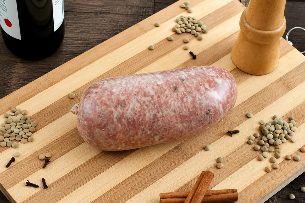 Homemade Cotechino resting on a wooden board with whole spices.
