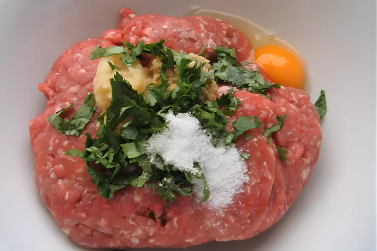 Raw lamb kofta mixture with egg, coriander, and spices in a bowl.