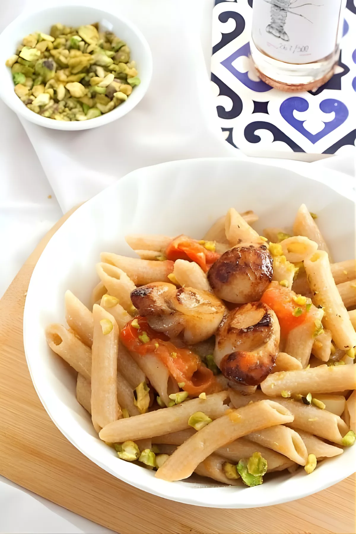 Bowl of pasta topped with seared scallops, cherry tomatoes, and crushed pistachios for Pasta with Scallops and Lobster Oil.