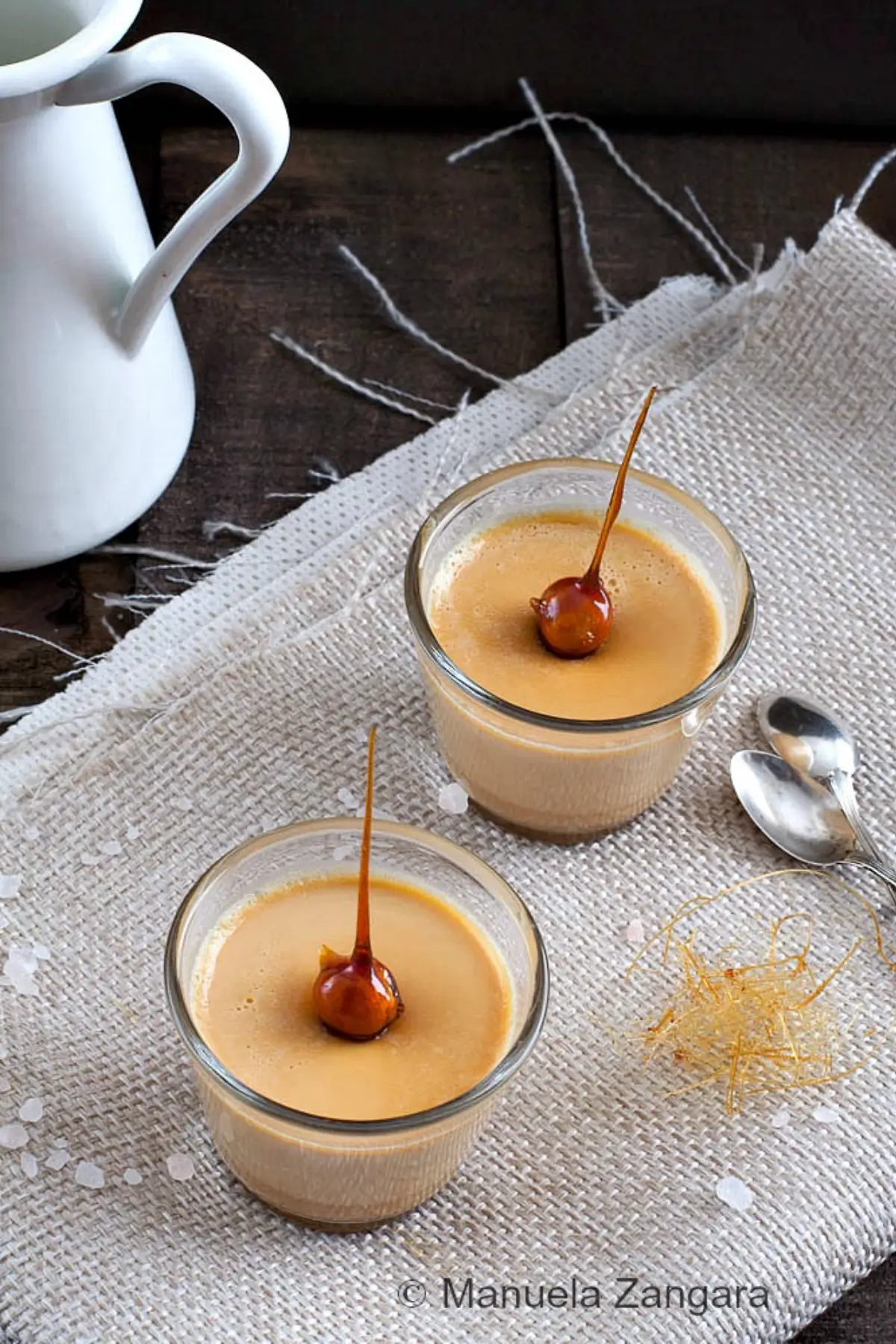 Two glasses of caramel panna cotta topped with caramel-coated hazelnuts.