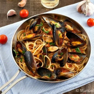 Spaghetti with Mussels in tomato and white wine sauce, garnished with parsley and cherry tomatoes.