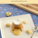 Molten white chocolate pudding dusted with icing sugar on a plate.