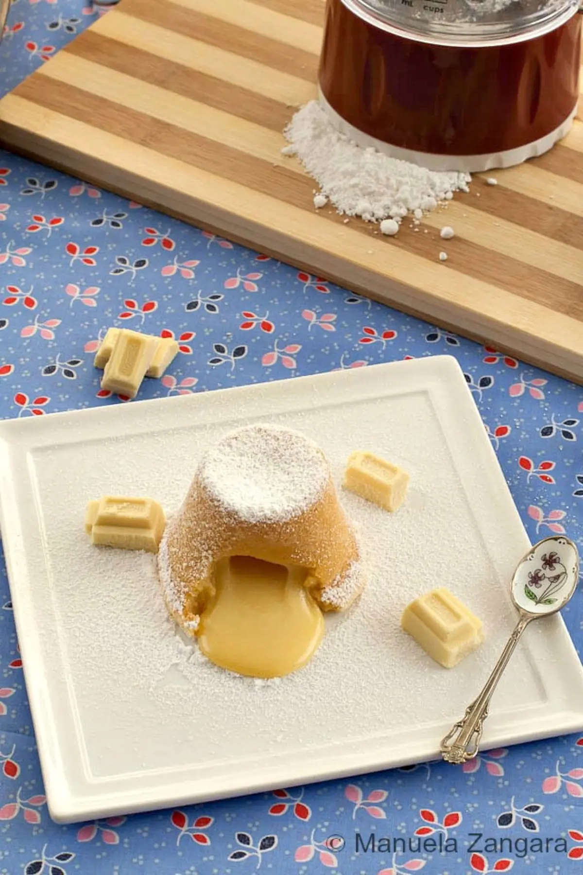 Molten white chocolate pudding dusted with icing sugar on a plate.