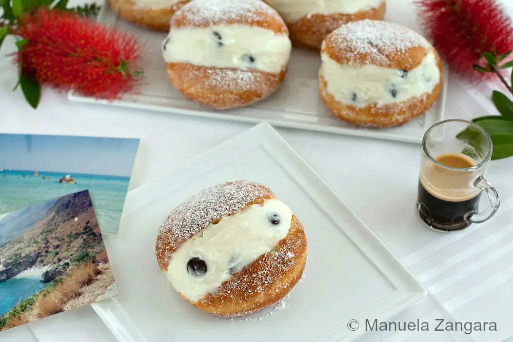 Single ricotta-filled doughnut dusted with icing sugar on white plate.