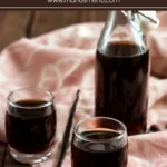 Bottle and glasses of vanilla coffee liqueur served with whole coffee beans and a vanilla pod on a soft cloth background.